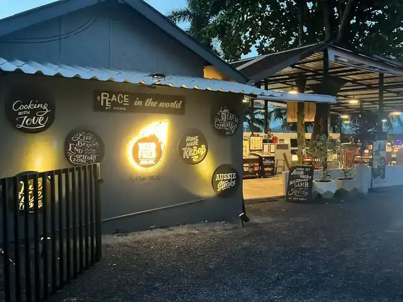 The front of the restaurant at dusk: a slate-grey wall with round signs and a lit logo, and the roofed dining room beyond