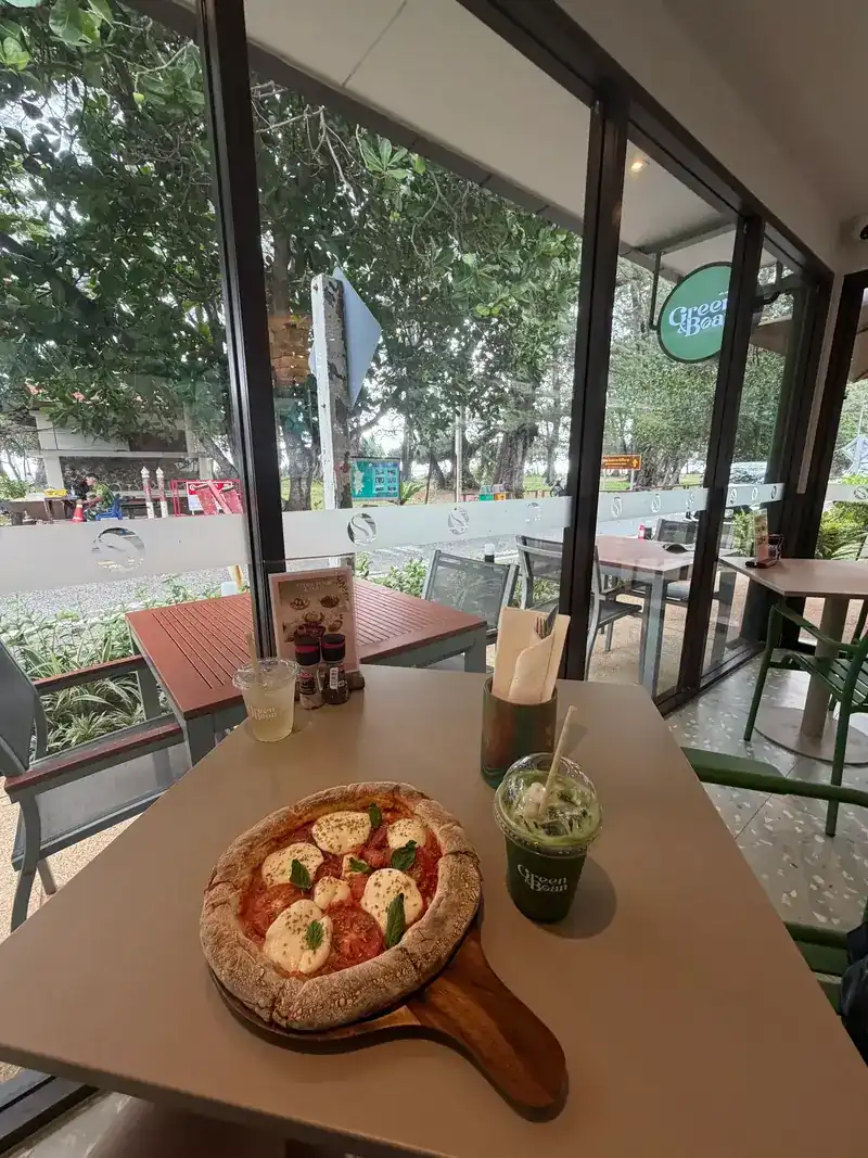 A Margherita pizza on a wooden board and an iced green drink, on a table by the window
