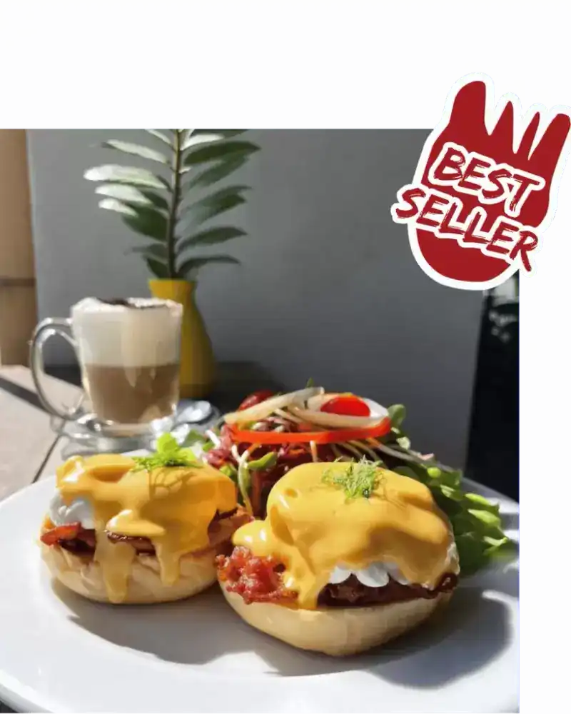 Two eggs Benedict under hollandaise with a salad and a glass of coffee