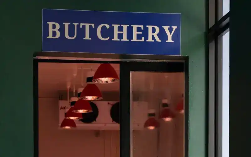 The blue Butchery sign above the glass door of the temperature-controlled butcher room, red lamps inside