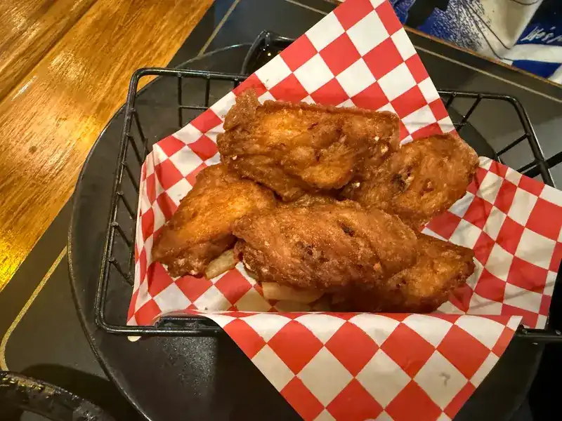 Fried chicken wings in a wire basket lined with red and white checked paper