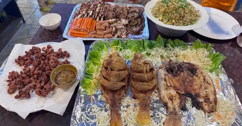 Fried and grilled fish on lettuce, skewers, fried rice and a dipping sauce laid out for one table