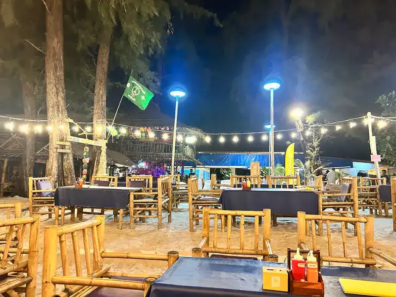 Bamboo tables on the sand at night, under the trees