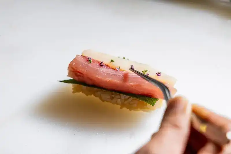 Tweezers placing shiso flowers on sliced fish over rice