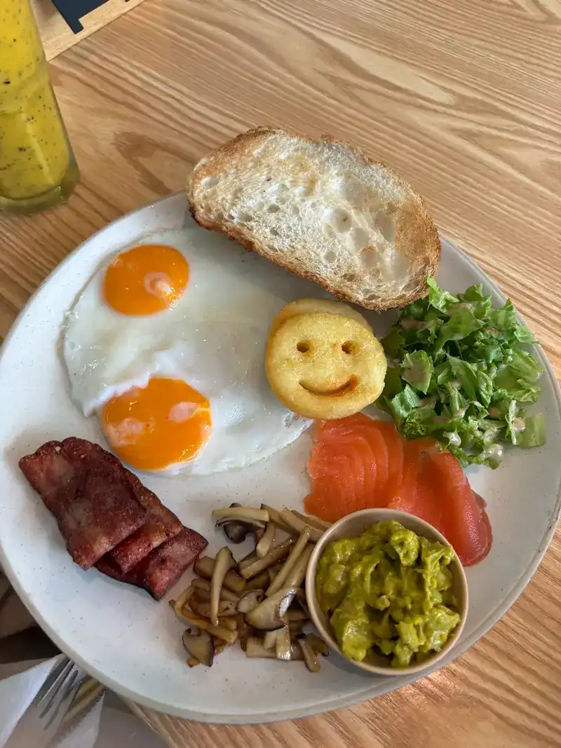 Fried eggs, a smiley potato, smoked salmon, bacon, mushrooms, salad and toast