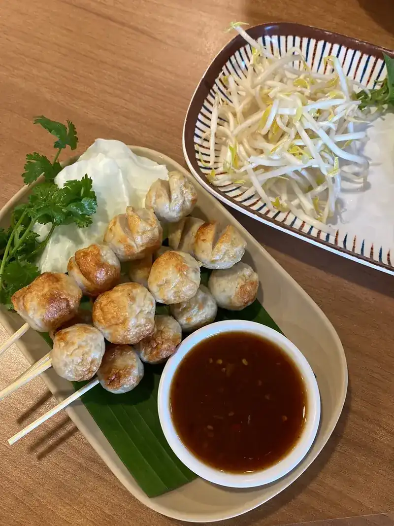 Grilled pork meatballs on skewers on a banana leaf, with a bowl of dipping sauce