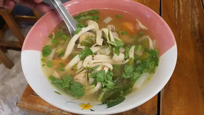 A bowl of soup with mushrooms, herbs and coriander, a spoon lifted from it