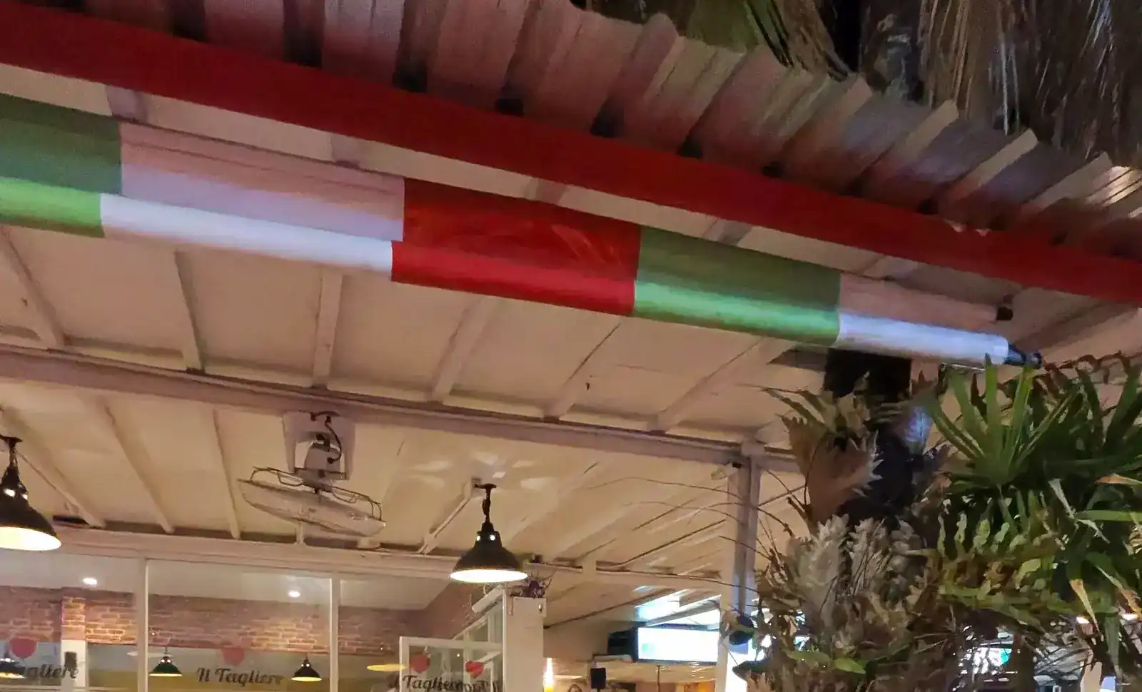 The terrace roof at night, its beam painted green, white and red, with Il Tagliere lettered on the glass below