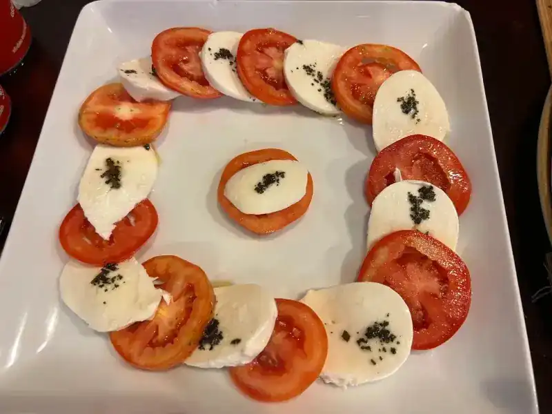 Caprese: slices of tomato and mozzarella arranged on a square white plate