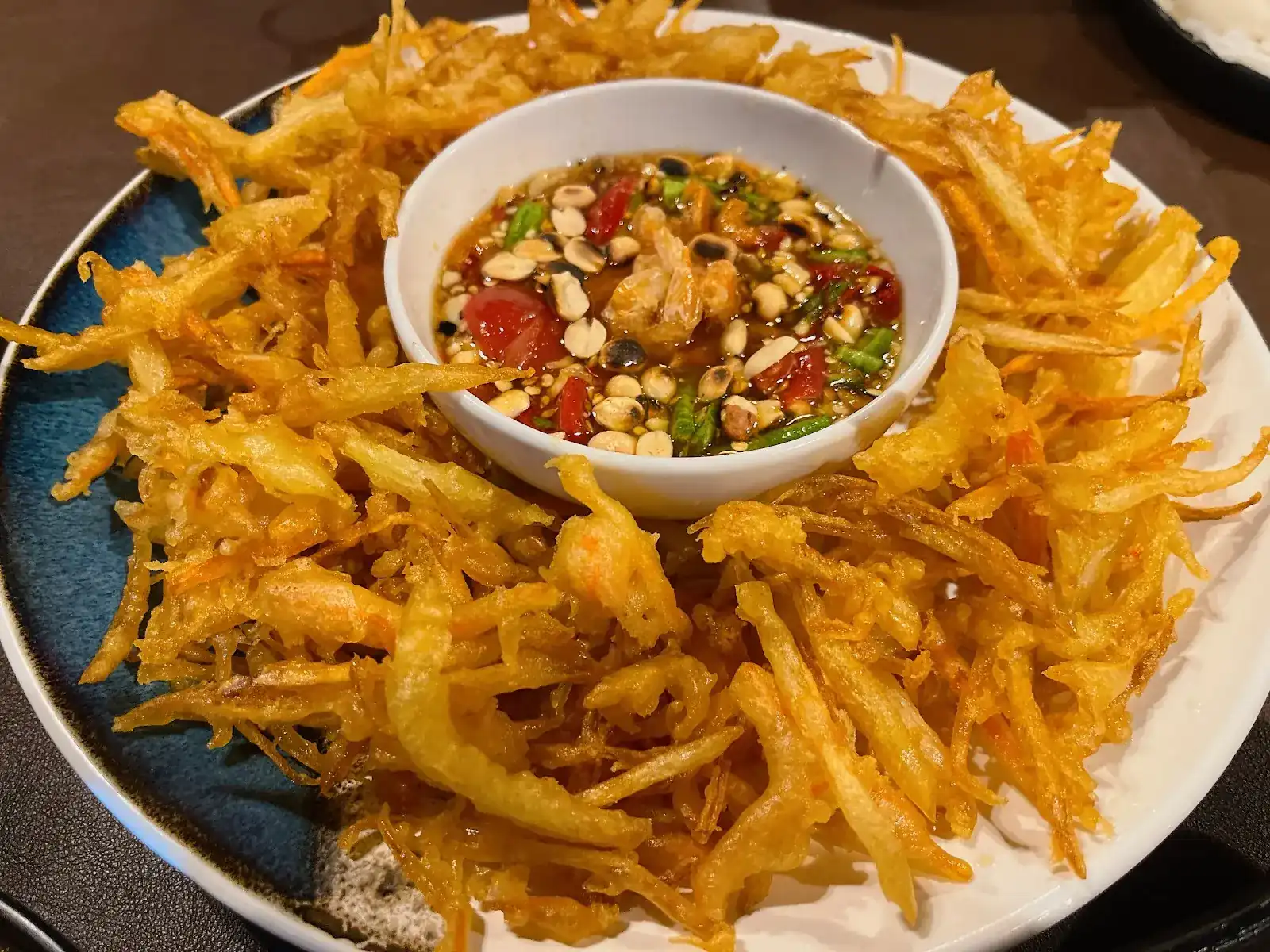 Crispy fried papaya salad around a bowl of spicy dressing with peanuts, tomato and shrimp