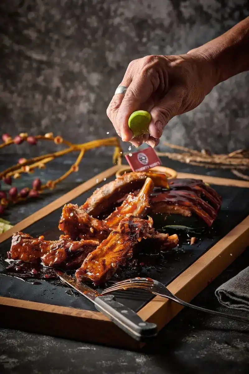 A hand squeezing lime over cut hickory ribs on a slate board