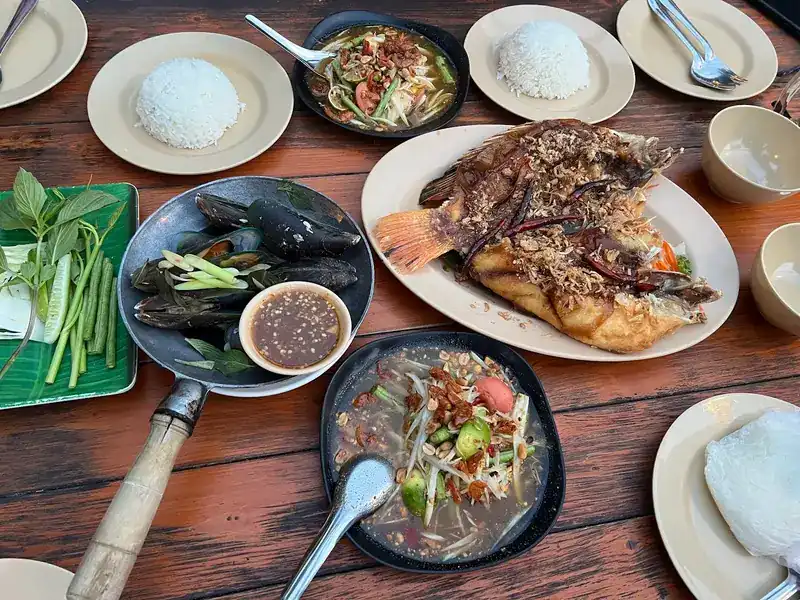 A shared table: papaya salad, mussels with dipping sauce, a whole fried fish and rice