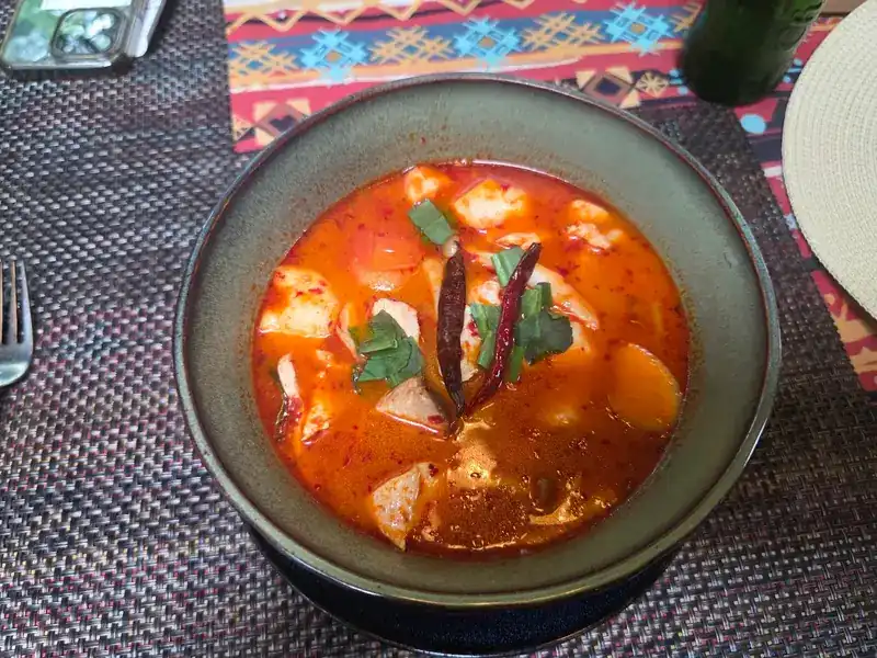 A bowl of red, spicy soup with dried chillies and herbs