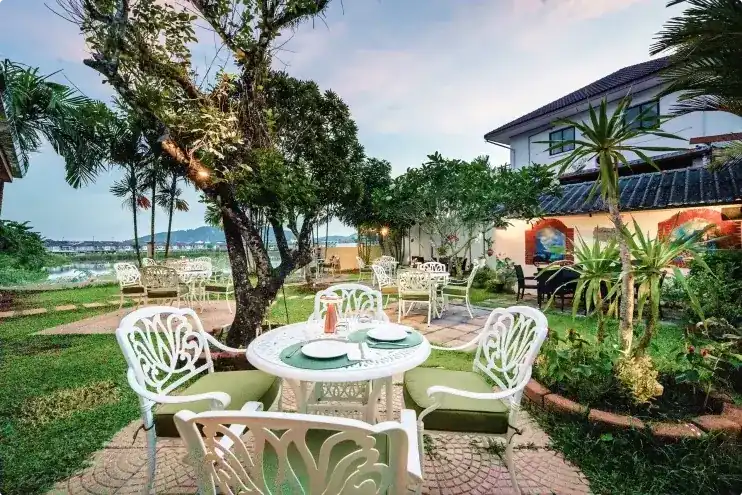 White iron tables on the lawn under a frangipani tree, with the lake and hills behind