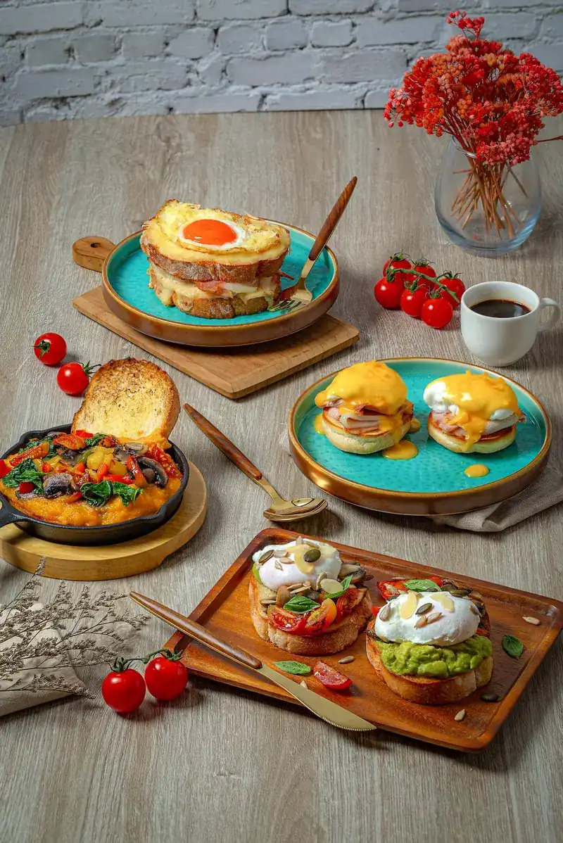 Croque madame, eggs Benedict with ham, a vegetable skillet with toast, and avocado toast with poached eggs on a wooden table