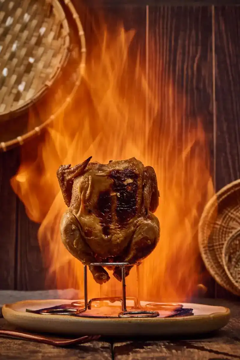 A whole chicken standing on a rack in front of open flames