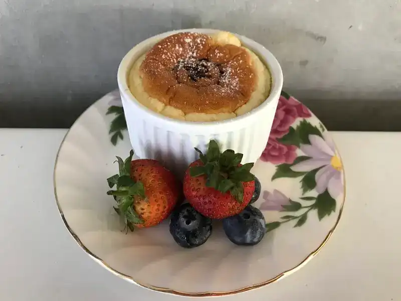 A soufflé in a white ramekin with strawberries and blueberries