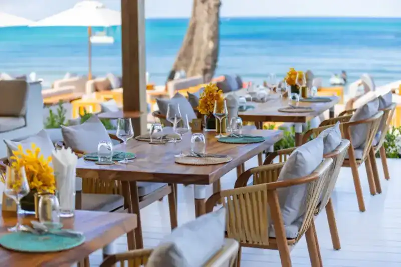 Wooden tables set with glasses and yellow orchids, the sea behind