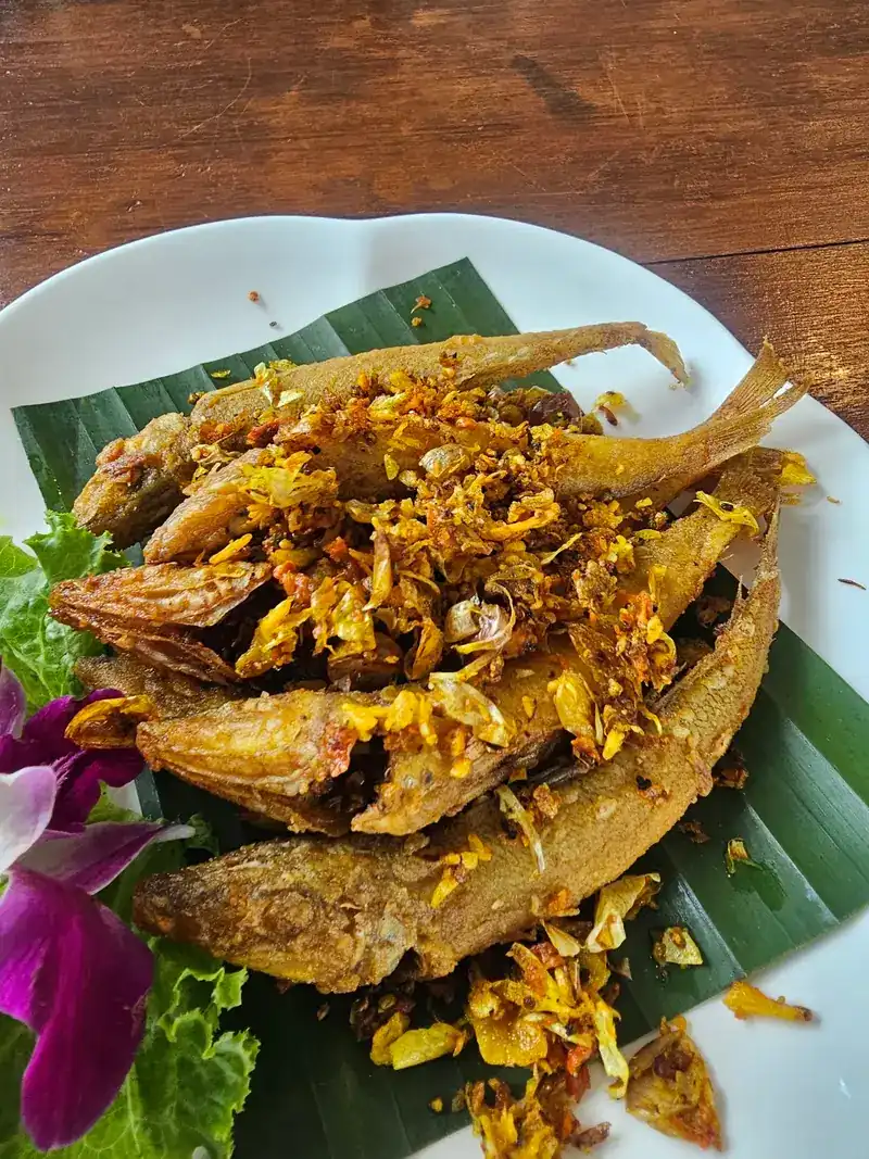 Small whole fried fish topped with crispy garlic on banana leaf