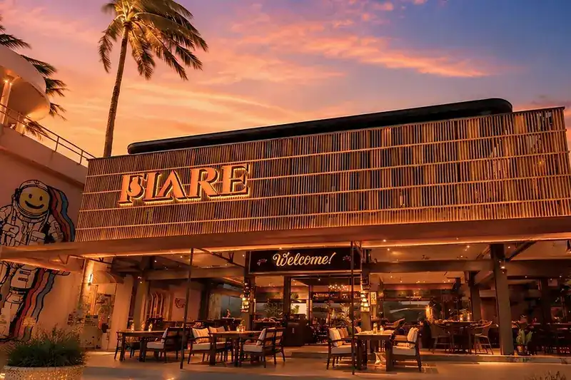 The FLARE building with its slatted wooden front, lit up under a pink sunset sky