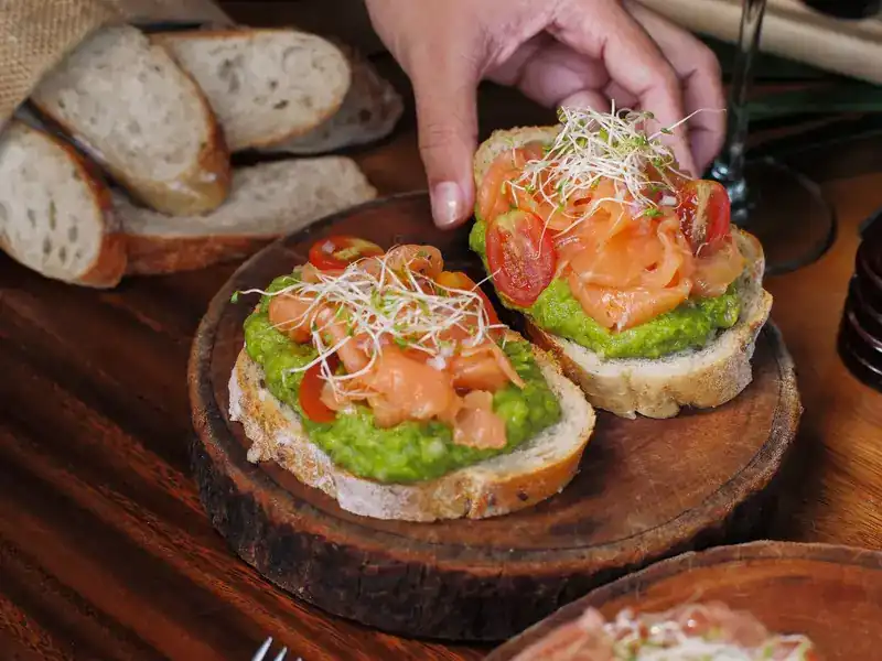 Toasted bread topped with avocado, salmon and tomato on a wooden block