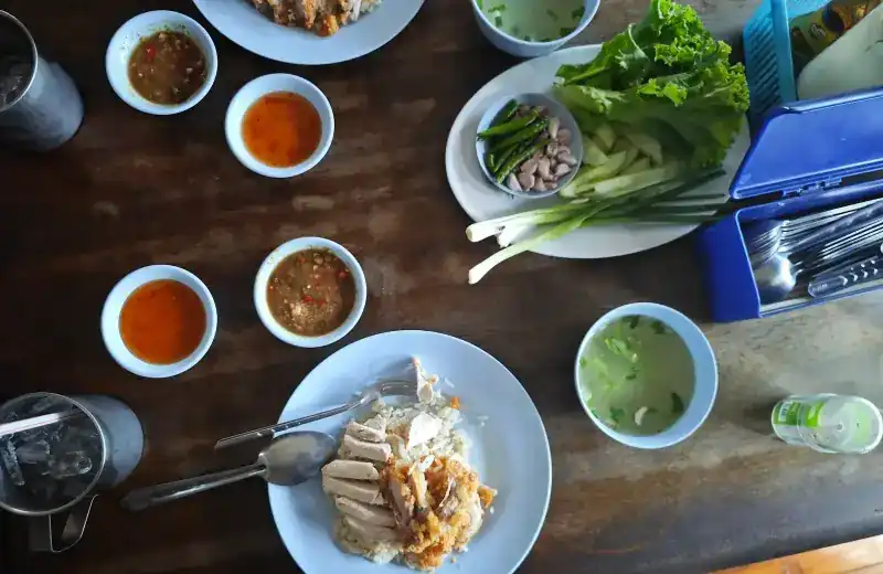 Chicken rice seen from above with clear soup, greens, spring onion and four small bowls of dipping sauce