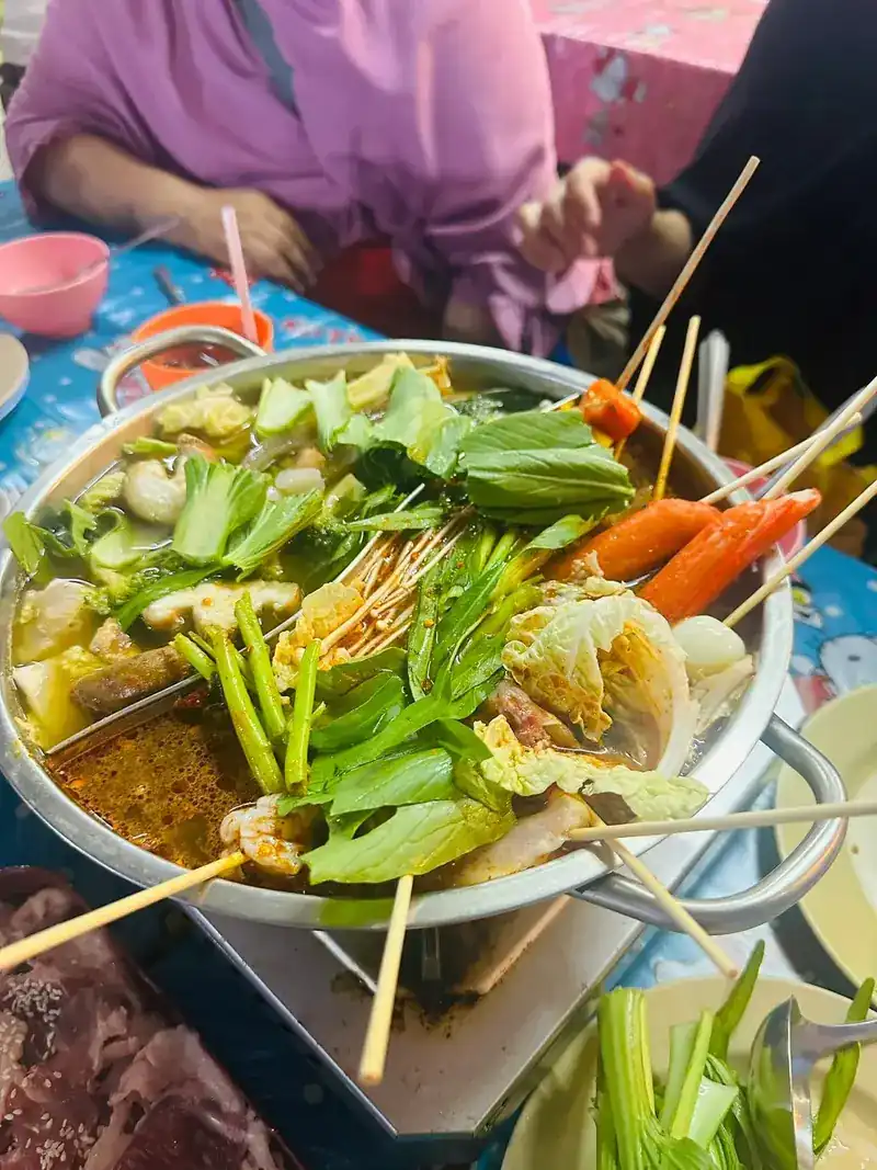 A hotpot full of greens and skewers on a table burner