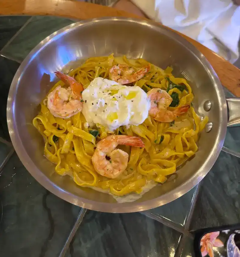 Ribbon pasta with prawns and a soft white cheese, served in the pan on a green tiled table