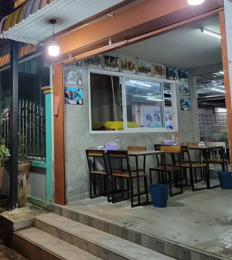 The open shopfront at night, wooden tables under hanging lamps / หน้าร้านยามค่ำ โต๊ะไม้ใต้โคมไฟ