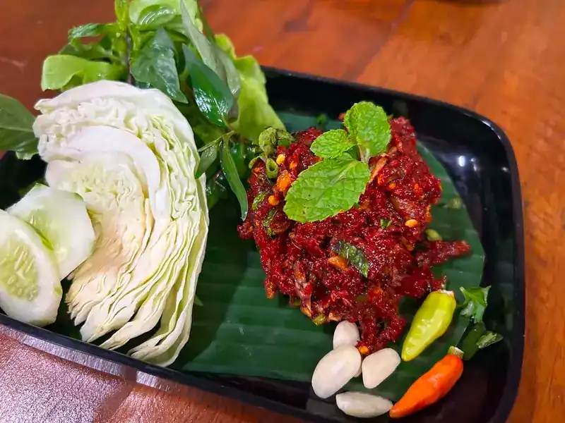 A chilli-red minced dish topped with mint on banana leaf, with cabbage, cucumber, garlic cloves and fresh chillies
