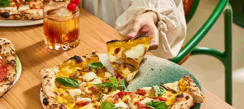 A hand lifting a slice of Pizza Giardiniera