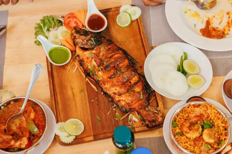 A whole grilled fish on a board with green chutney, lime and prawn rice