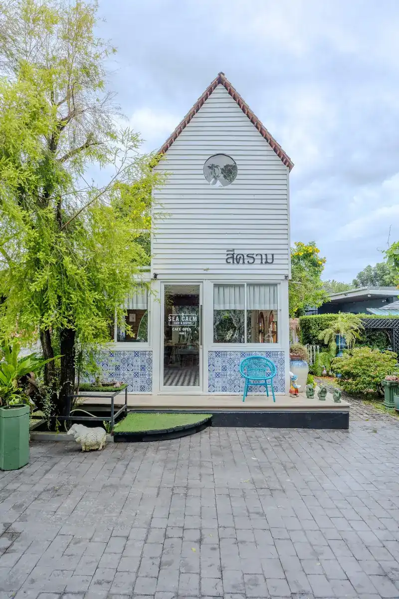 The front of the white wooden house, with สีคราม written on it and blue-and-white tiles at its base