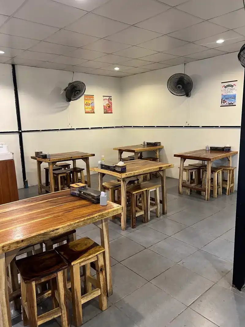 Inside the shop: wooden tables and stools on a tiled floor, fans on white walls
