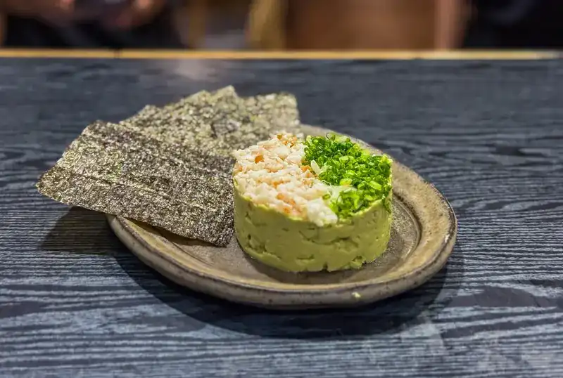 A round of avocado topped with spring onion, served with sheets of crisp nori