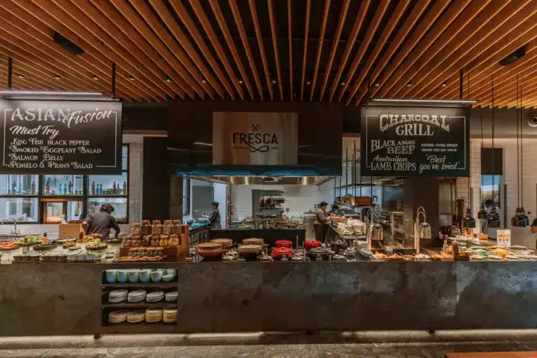 The open kitchen counter at Fresca under a timber-slat ceiling, with chalkboards for Asian Fusion and Charcoal Grill