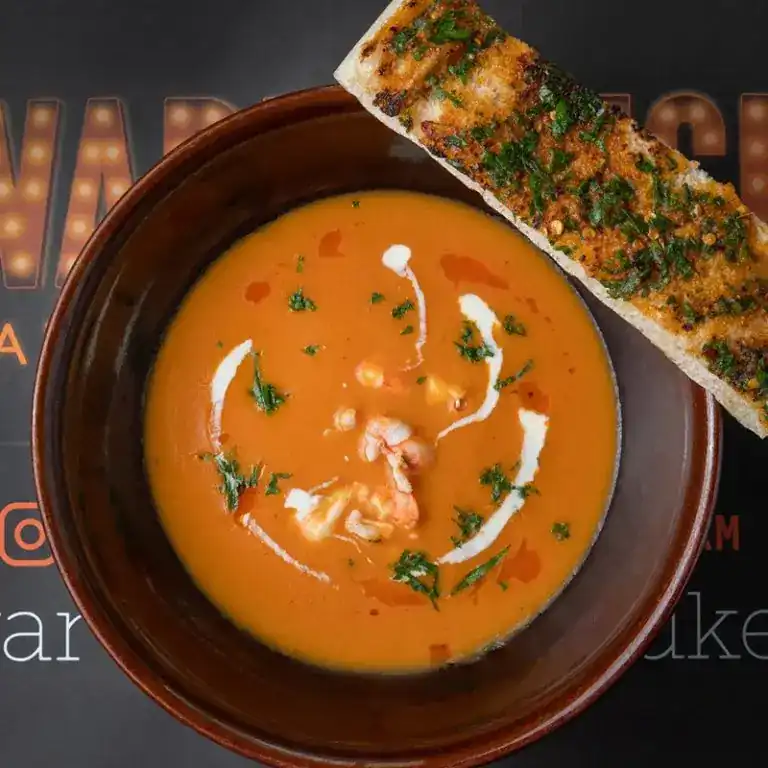 A bowl of orange seafood soup with prawns, cream and herbs, garlic toast on the side