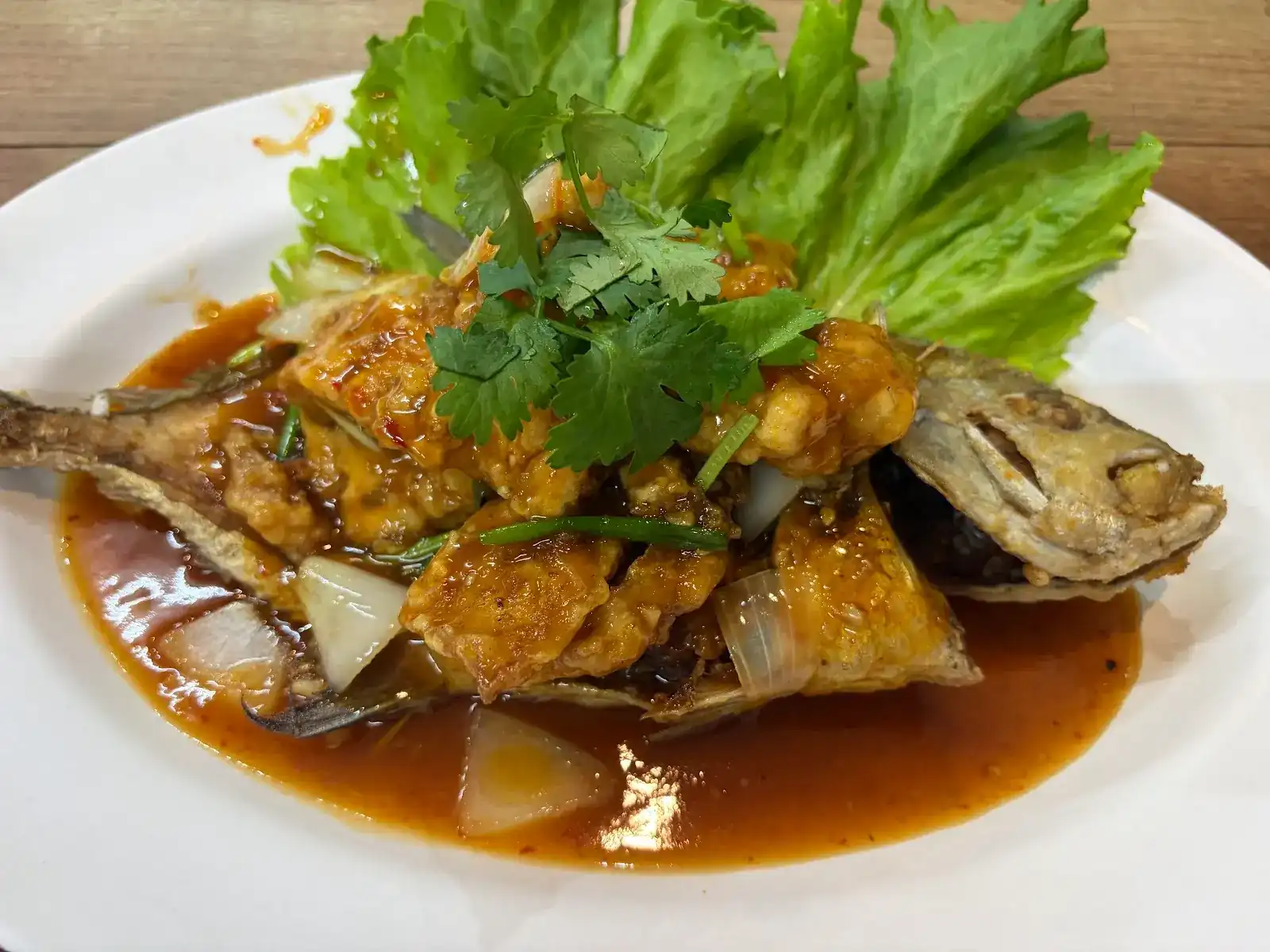 A whole fried fish under a glossy red sauce, topped with coriander, with lettuce leaves