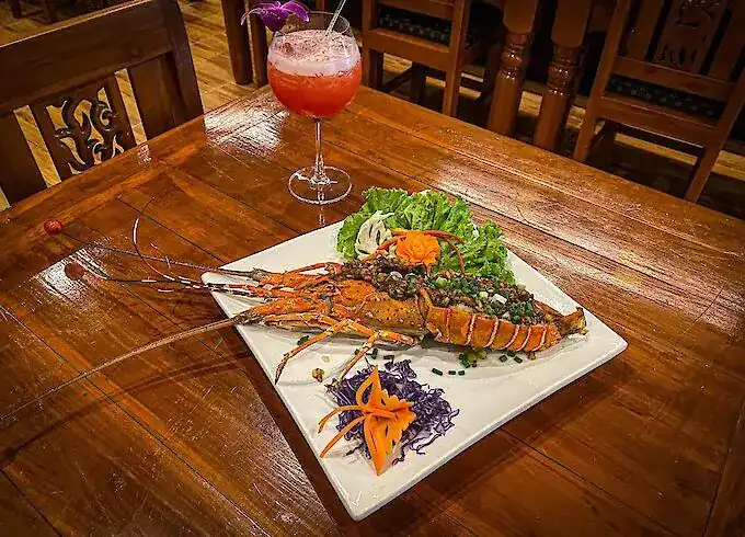 A whole lobster with garlic on a white plate, on a carved wooden table in the dining room