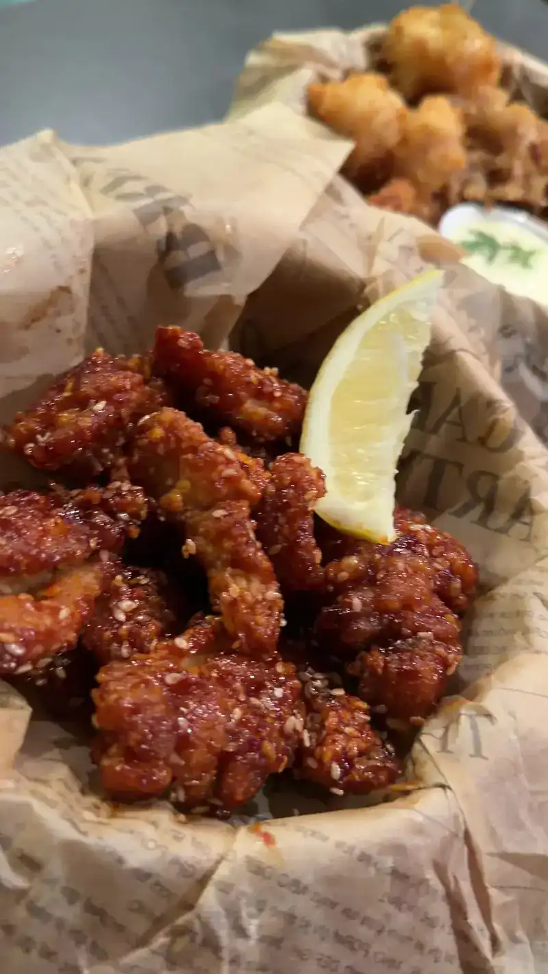 Korean fried chicken with sesame and a lemon wedge in a paper-lined basket