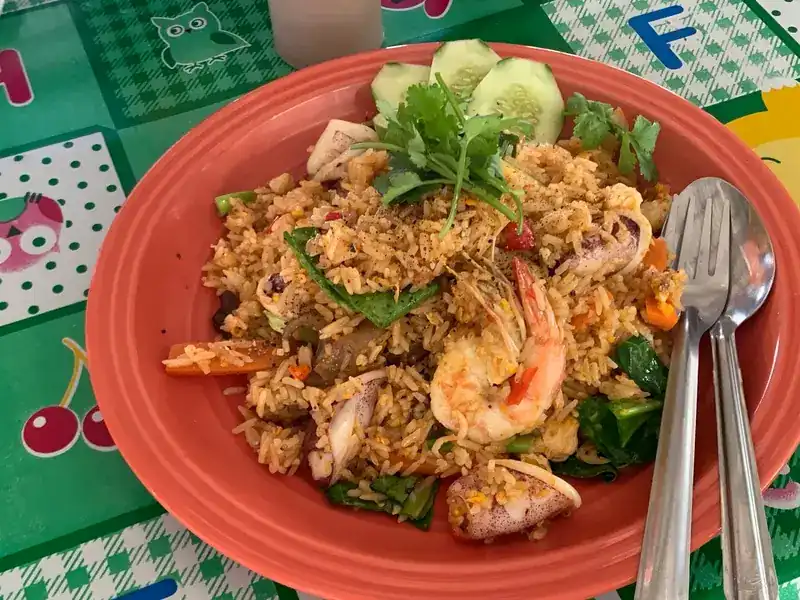 Fried rice with prawns and squid, cucumber slices and coriander, on an orange plate on the green oilcloth table