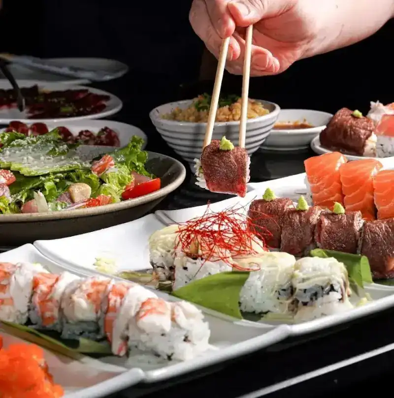 Salmon rolls, prawn rolls and rolls topped with beef, one piece lifted with chopsticks