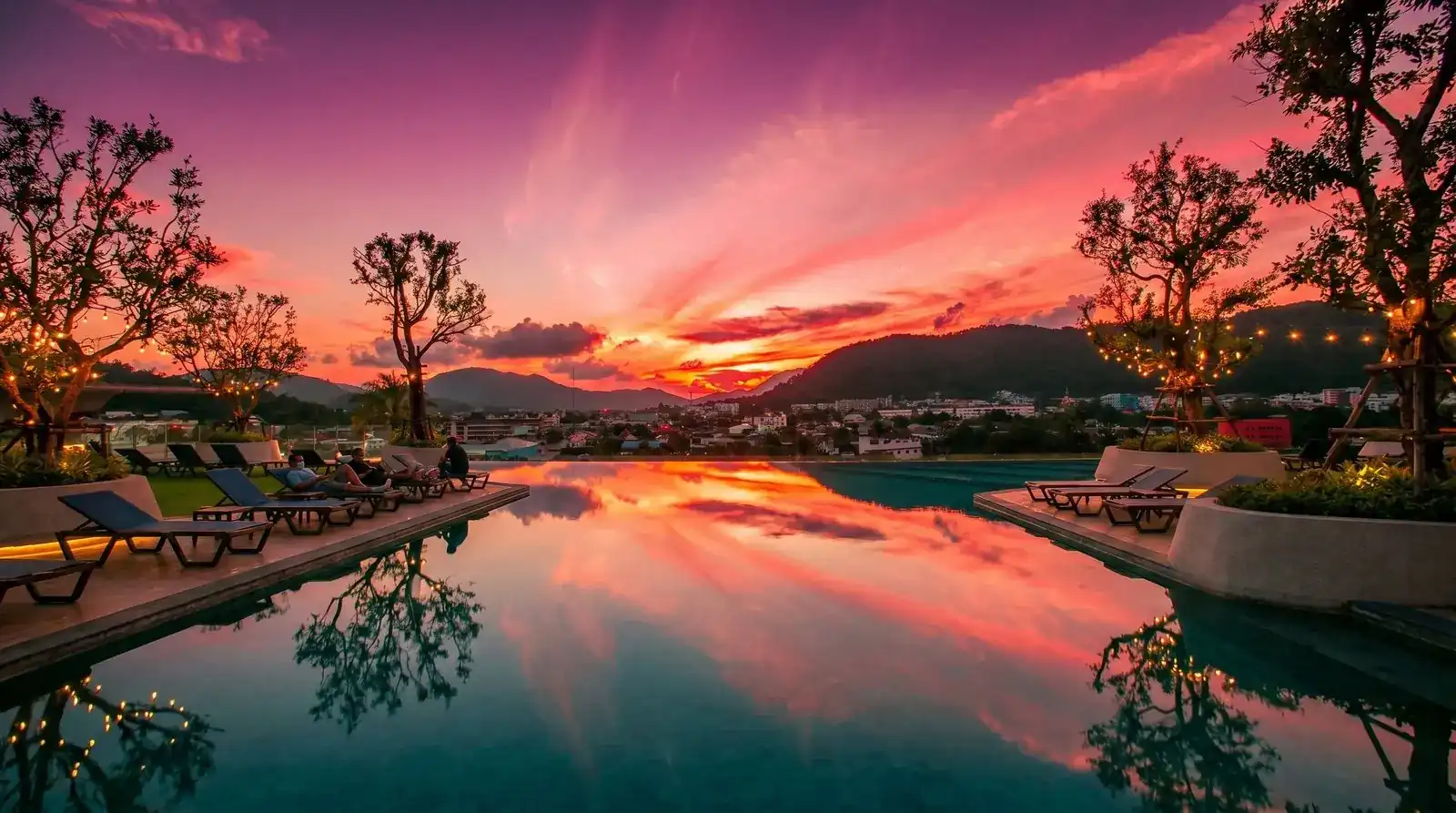 The rooftop infinity pool at sunset, reflecting a pink sky over the hills of Phuket Town