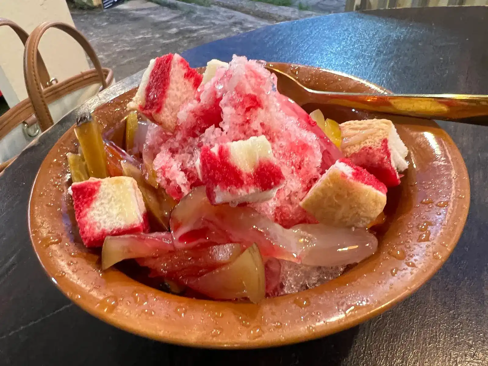 Shaved ice with red and white cubes, fruit and syrup in a brown bowl
