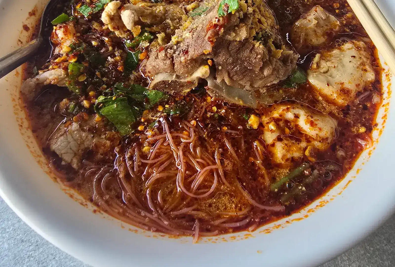 Tom yum noodle soup: thin rice noodles, meat, chilli and peanuts in a red broth