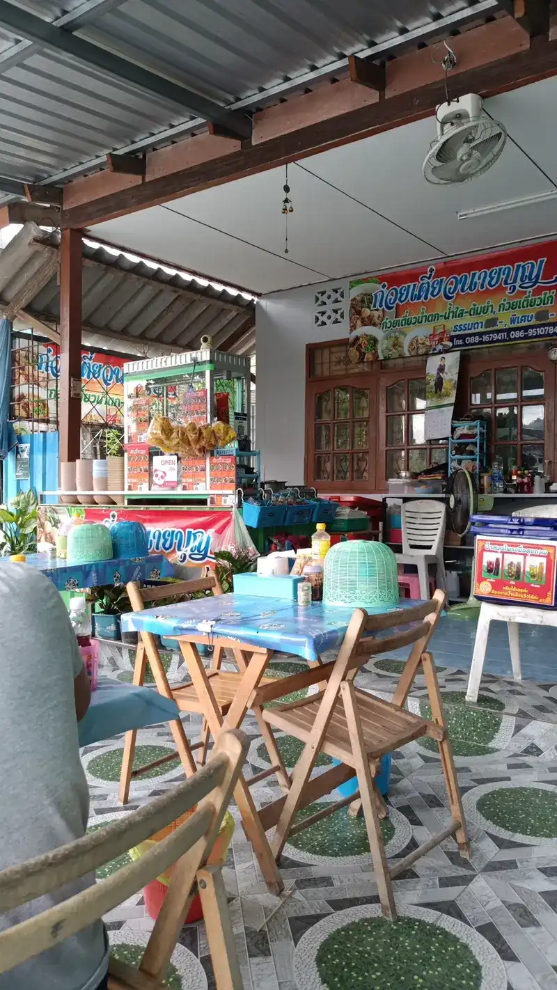Inside the shop: wooden folding chairs, blue tablecloths, a patterned tiled floor and a fan under the roof