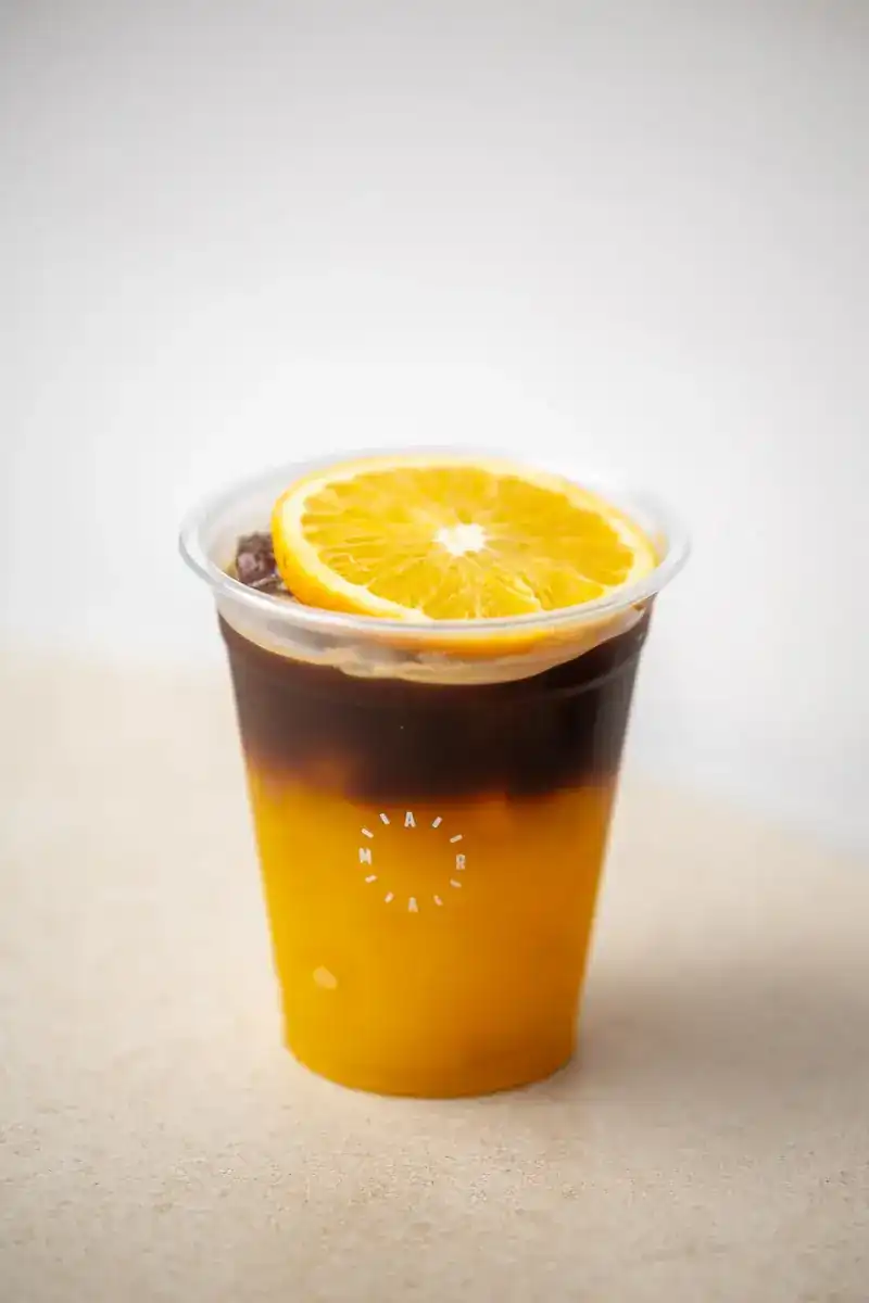 Black coffee over orange in a cup printed with the Aram ring, topped with an orange slice
