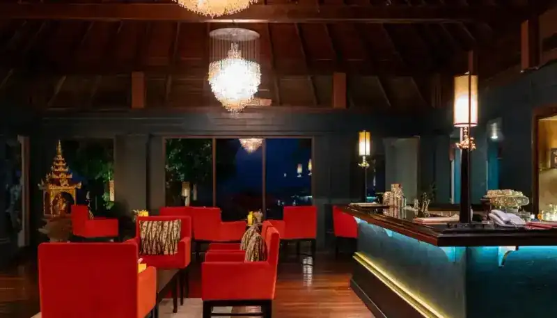 The bar and lounge: red velvet chairs under crystal chandeliers, a teal-lit counter