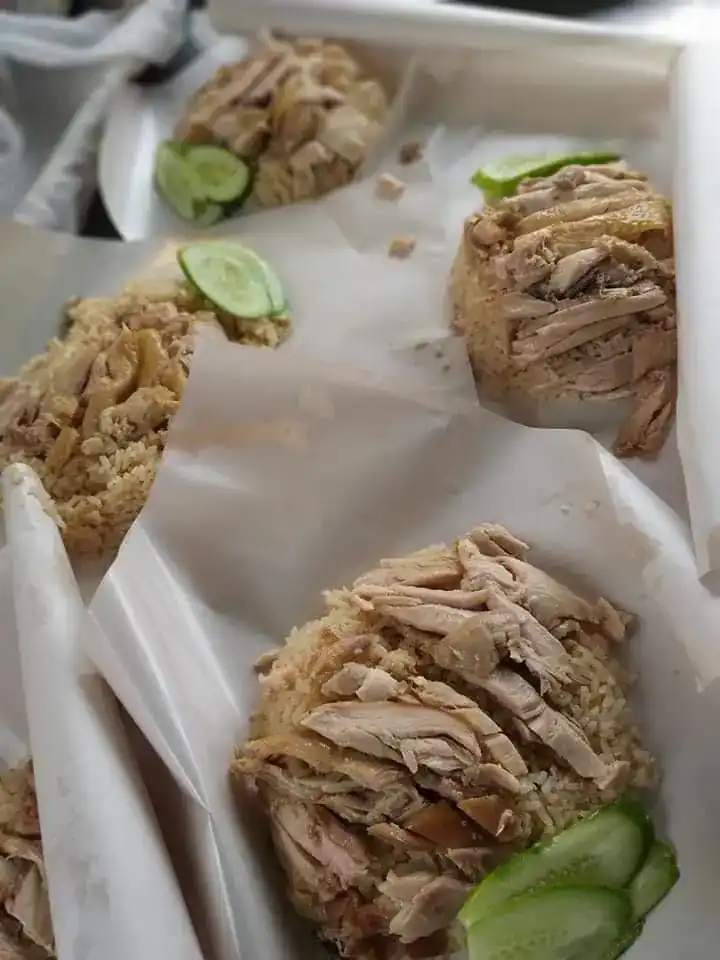 Rice topped with pulled chicken and cucumber slices, served on paper