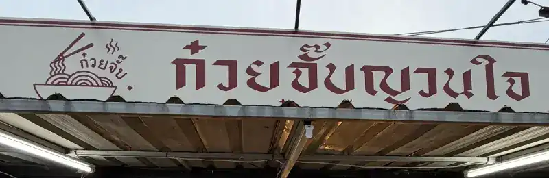 The shop sign: ก๋วยจั๊บญวนใจ in claret letters beside a noodle-bowl drawing